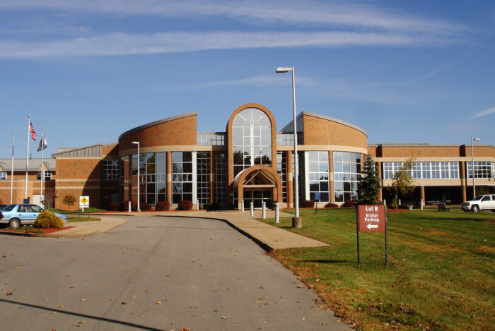 A large brick building is shown, featuring large windows and can be seen against a blue sky.