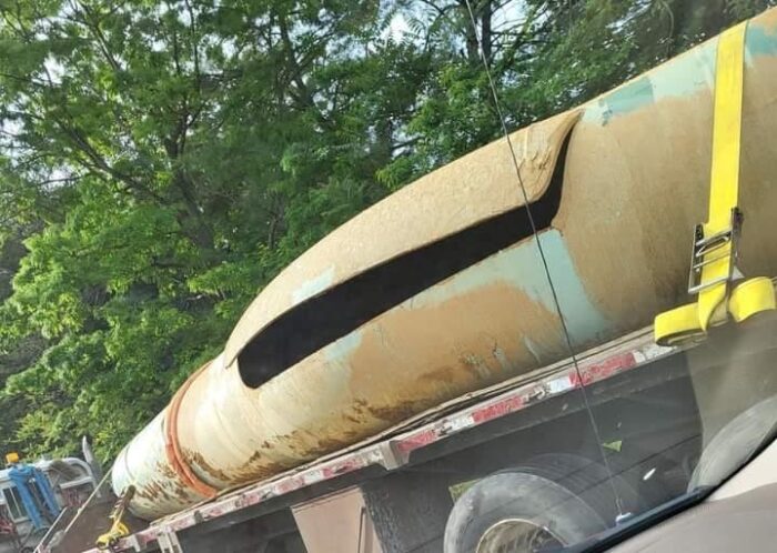 A section of damage pipe secured to a flatbed truck, pictured from inside someone's car.