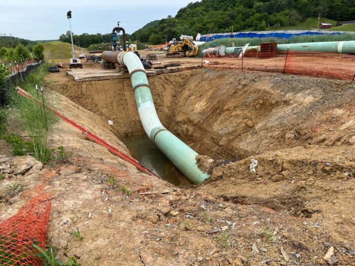 A faded green pipe emerges from a puddle of water in the excavated ground, surrounded by construction equipment.