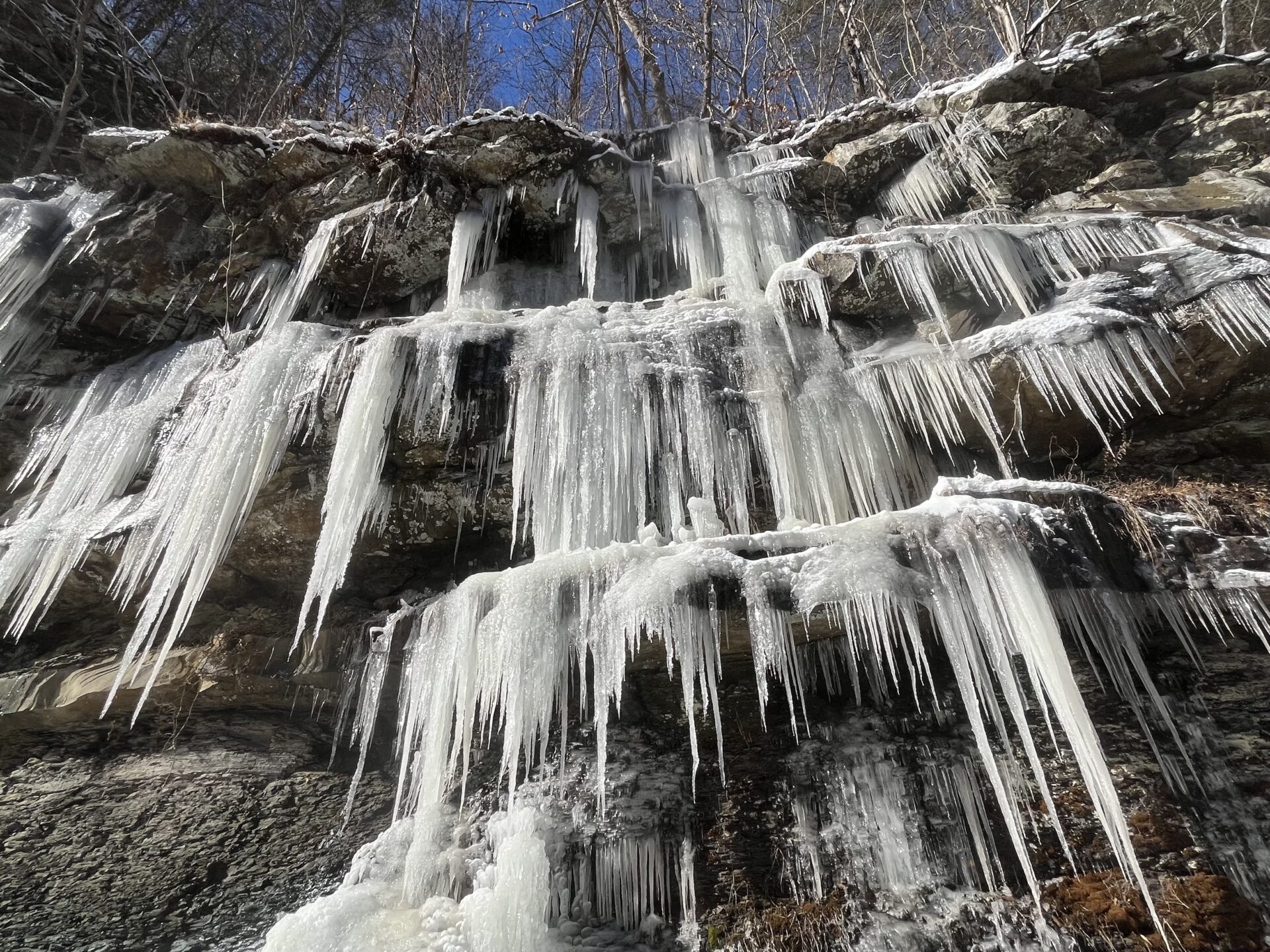 Icicles poke out from layers of a rock formation that form a small cliff on the side of the road.