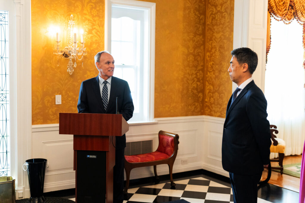 Two men in a brightly lit room wearing dark, formal suits.