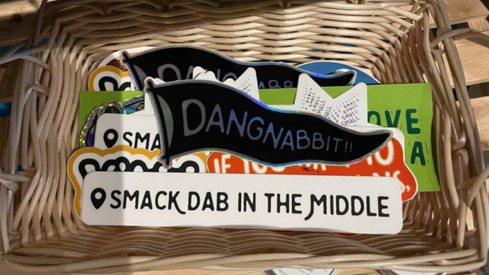 A pile of stickers are seen in a basket. One sticker reads, "Dangnabbit," and another reads, "Smack dab in the middle."