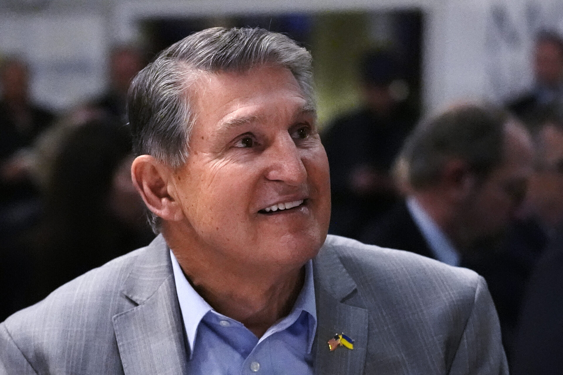 An older man with salt and pepper hair looks off camera smiling. He wears formal clothing.