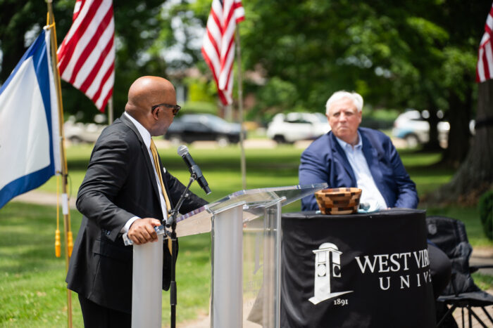 Two men sitting, one in front of the podium another watching.