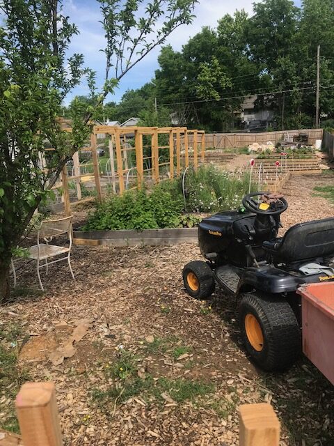 A tractor is shown parked just outside a garden. It is a sunny day and the vegetation looks green and vibrant.