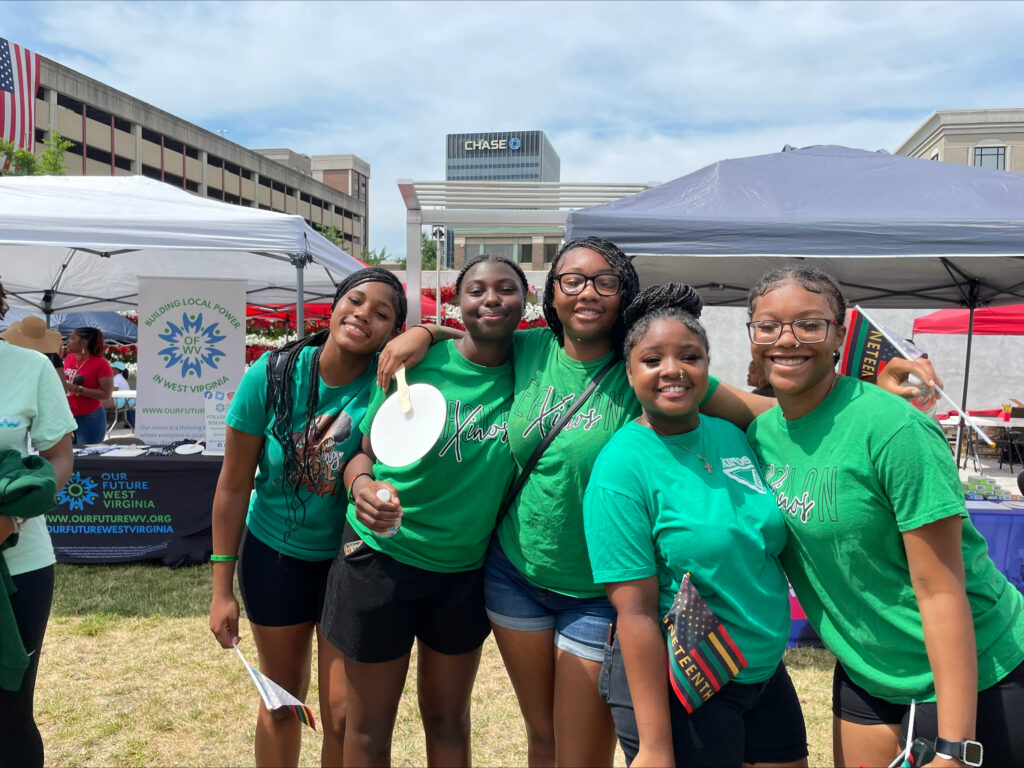 Five girls in green shirts stand and pose for a photo.