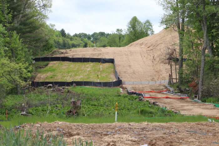 Evidence of pipeline construction including erosion control fences and recently seeded grass, surrounded by trees on both sides.