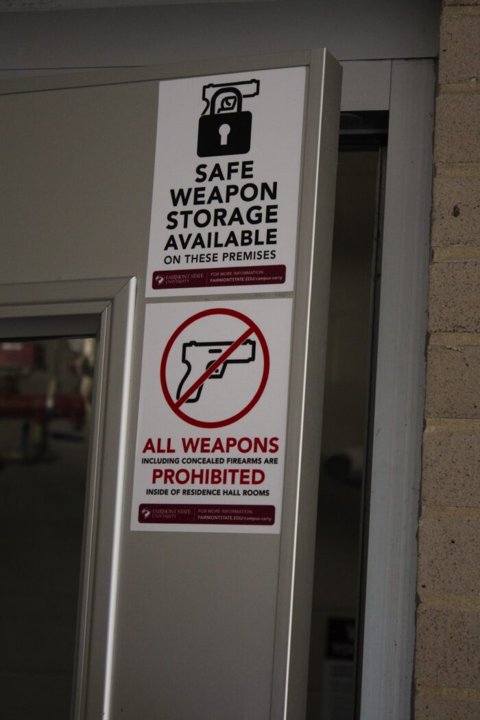 Stickers on a slightly ajar metal door read "Safe Weapon Storage Available" below a simple black vector image of a lock over the outline of a handgun and "All Weapons Prohibited" below an outline of a handgun inside of a red circle with a line through it.