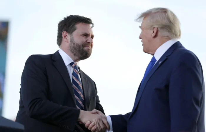 Two men shake hands on a stage. Both are dressed in business suits.