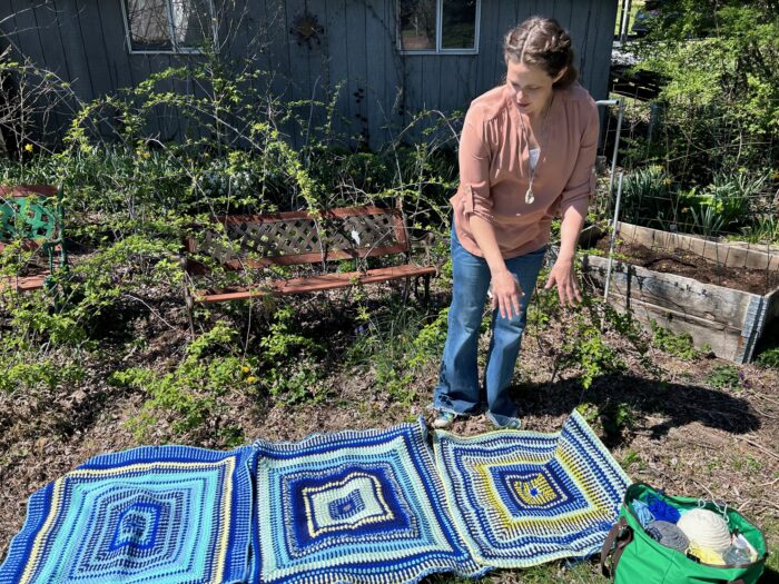 Ciera Pike shows off the individual large squares of a multi-colored blanket next to her garden.