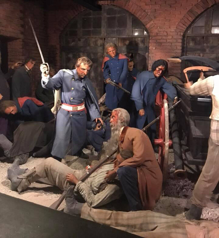 Several different wax figures of men in military uniforms are posed as if engaging in combat. A man in the foreground has his sword drawn and is looking at a man with a long beard who is squatting down to hold up a fallen soldier. Other men in military uniform fight behind them, and a canon is visible to their side.