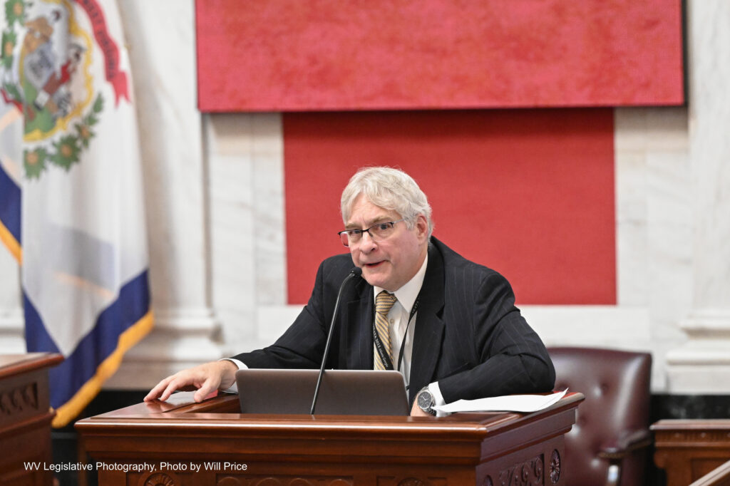 Man with white hair in a dark suit behind a lectern