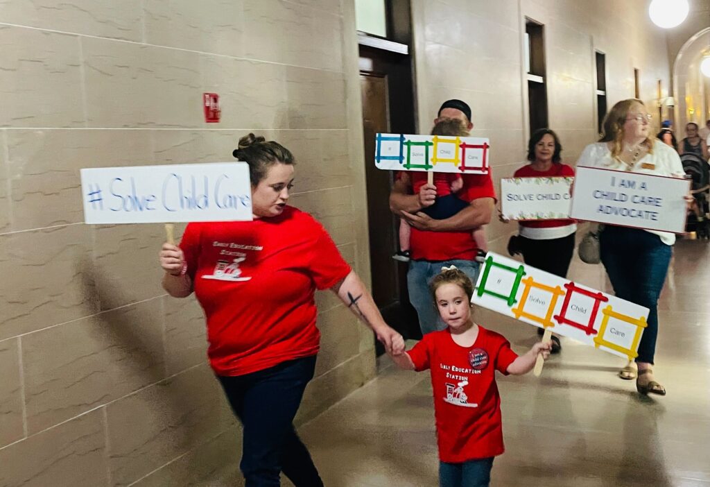 Adults and children walk through the halls holding signs.