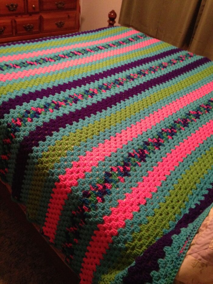 A colorful crocheted blanket covers a bed.