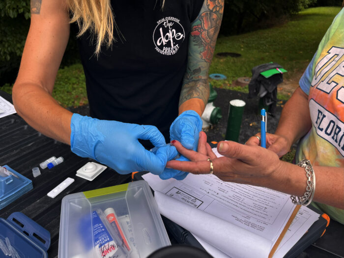 Woman wearing medical gloves draws a drop of blood for mobile HIV testing.