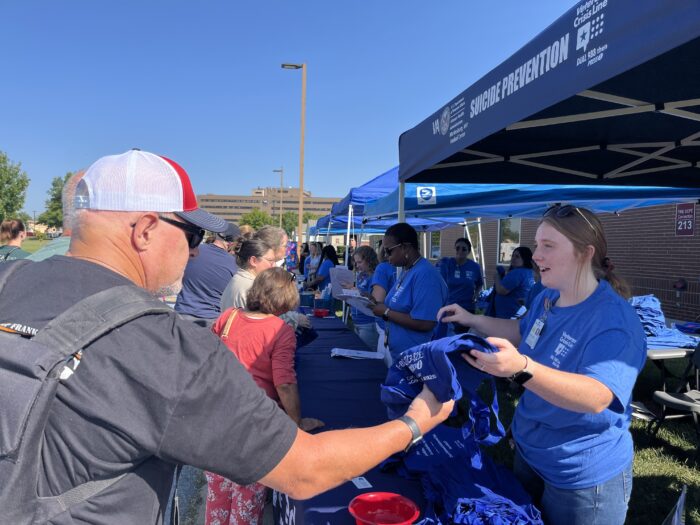 People line up alongside tents and receive t-shirts and other merch from volunteers wearing blue shirts.