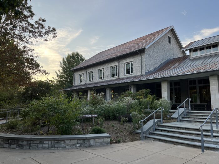 A stone-brick building with a rusty metal roof sits before a sunset. It has a garden and stone stairway out front.