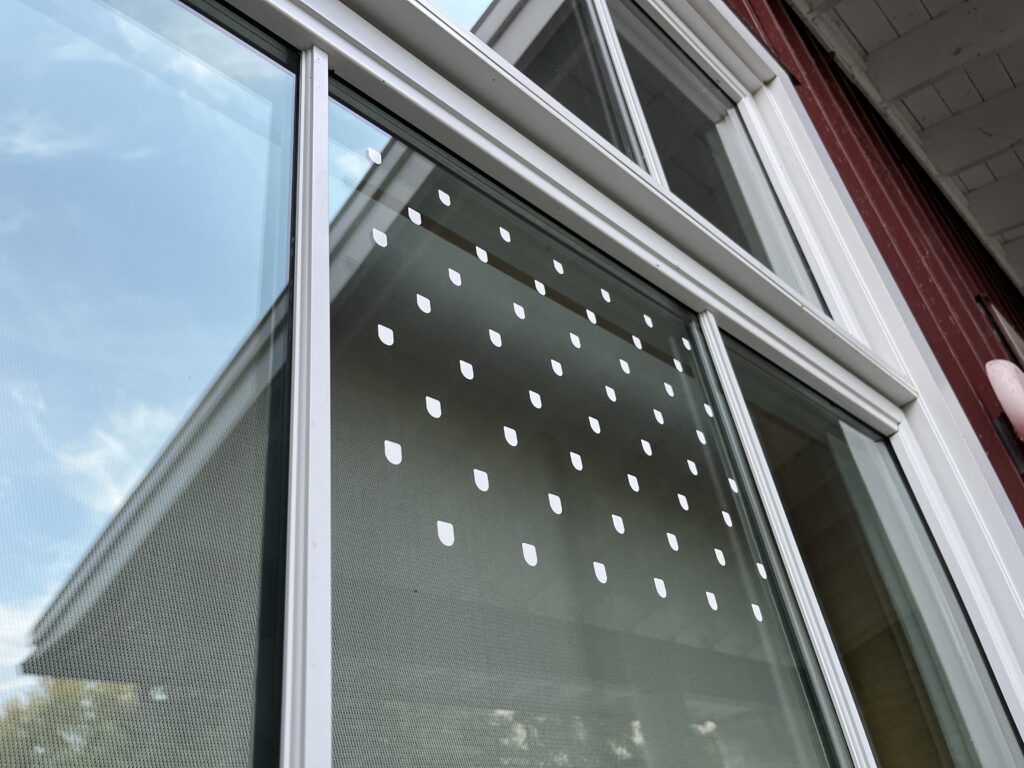 A red building has large, white-paned windows. Part of one of these windows has several U-shaped white stickers pasted onto it.