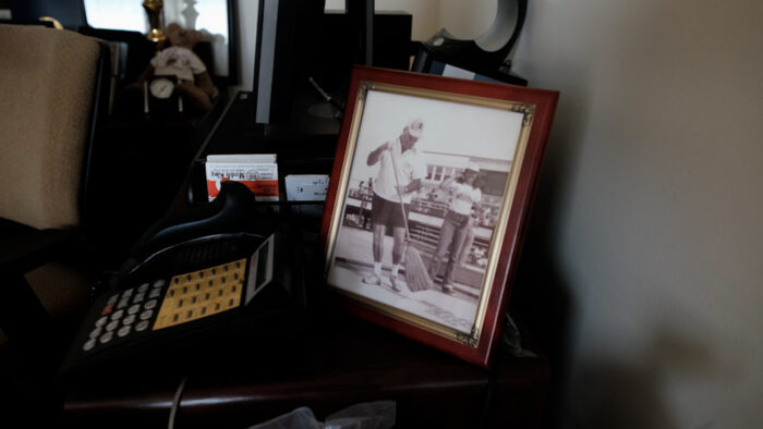 A framed black and white photo of a man sweeping with a broom sits on a desk next to a phone,