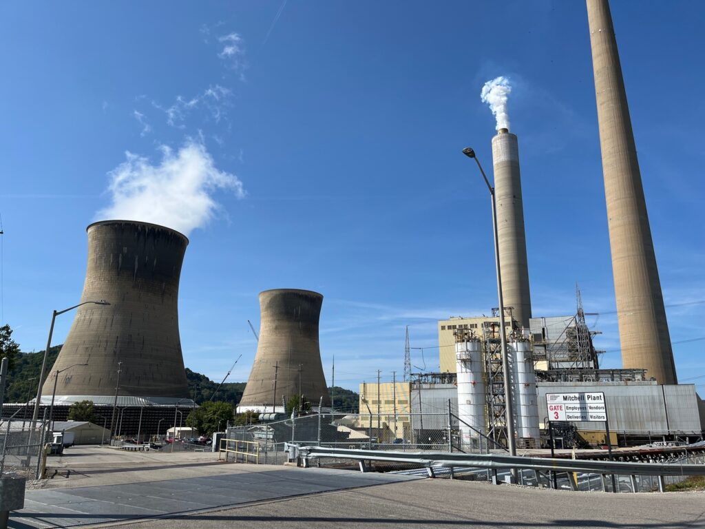 Concrete cooling towers and smokestacks loom over a power plant site against a clear sky with a trace of water vapor entering the air.