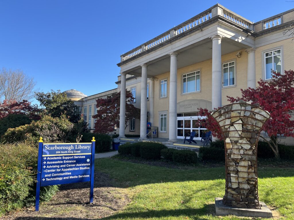 A tan-colored building with four columns and many windows is labeled "Scarborough Library" with text etched above the doorway.