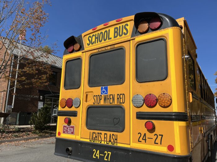A yellow school bus viewed from the rear sits outside a brick building labeled "Shepherdstown Town Hall."