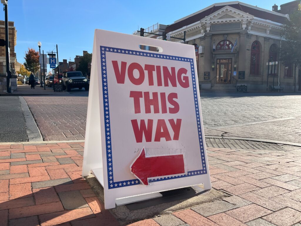 A sign on a brick city street reads "Voting This Way" with an arrow pointing left.