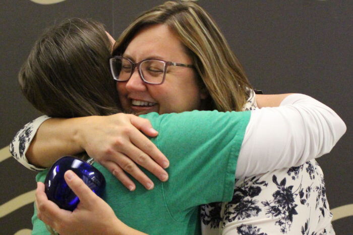 A woman with brown hair and glasses is hugging another woman with brown hair.