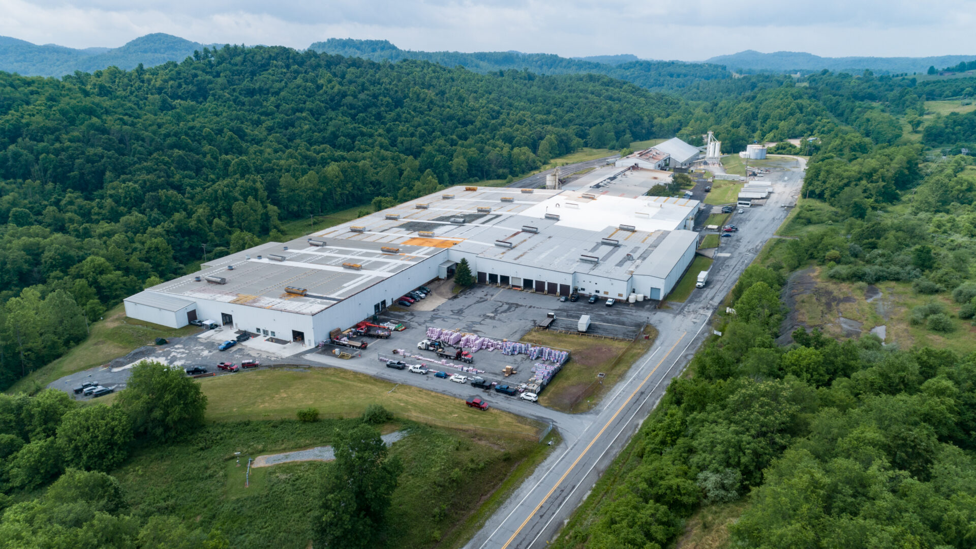 An overhead view of a factory site surrounded by lush green foliage on an overcast day.