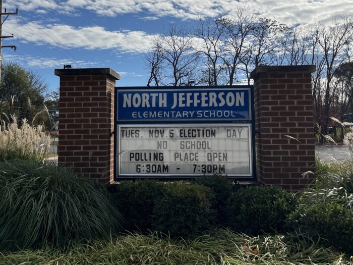 A blue and white school sign reads "North Jefferson Elementary School." Below it is a black and white inscription "tues Election Day November 5, no school, polling stations open 6:30 a.m. to 7:30 p.m."