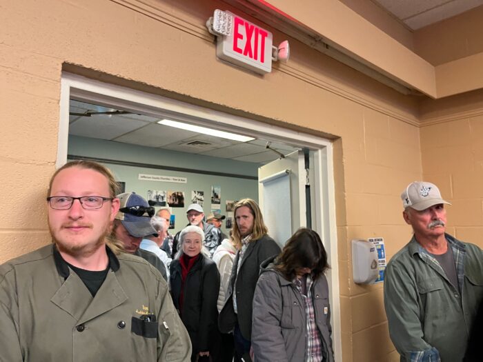 People crowd along a doorway to a brick room, tapering into the hallway.