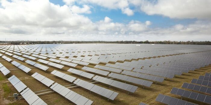 A field of solar panels beneath a partially cloudy sky.