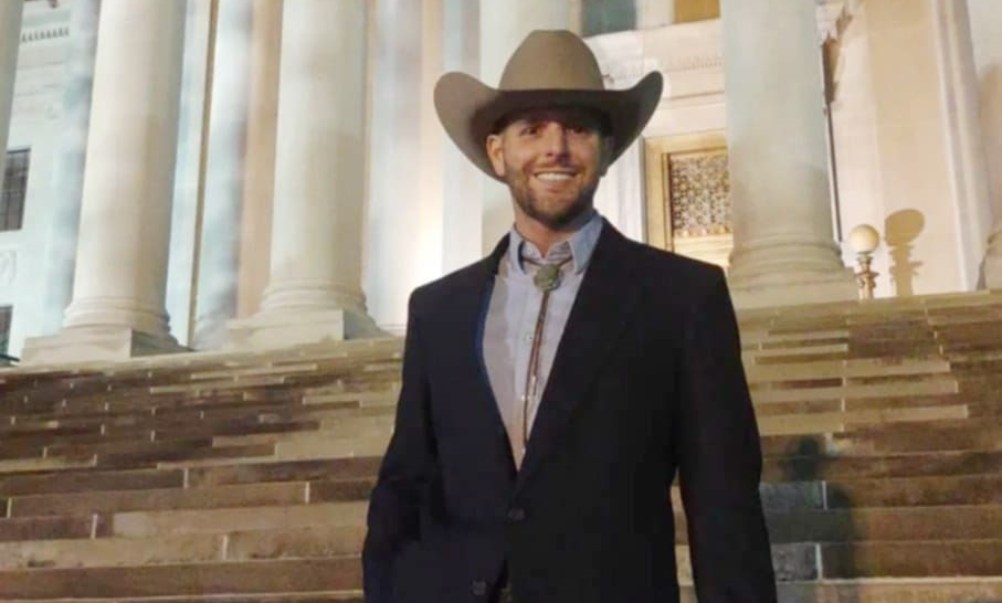 A man stands with a cowboy hat smiling.