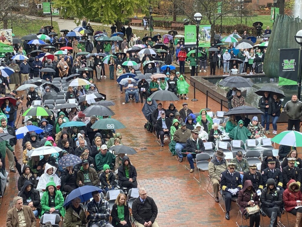 Large outdoor crowd seated in rain, many with umbrellas