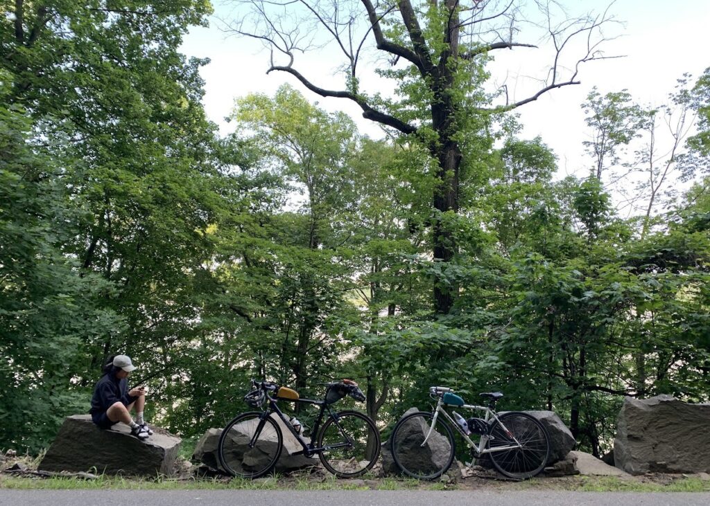 A woman looks at her phone as she sits on a rock next to two bicycles.