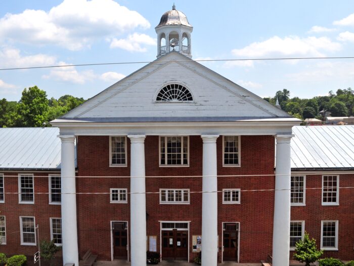 A red brick building with four white columns in front of it, in a picture from above.
