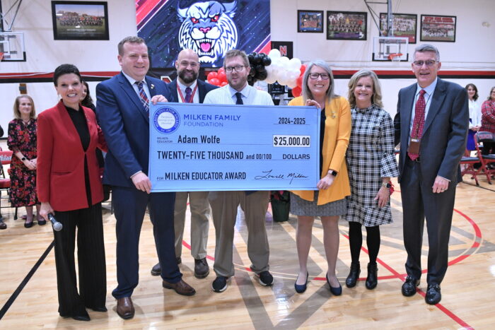 A group of seven people pose with an oversized check for $25,000.