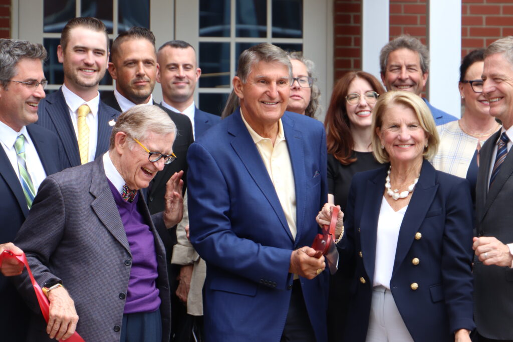 Three officials, two men and one woman, cut a ribbon for a project with others smiling behind them.