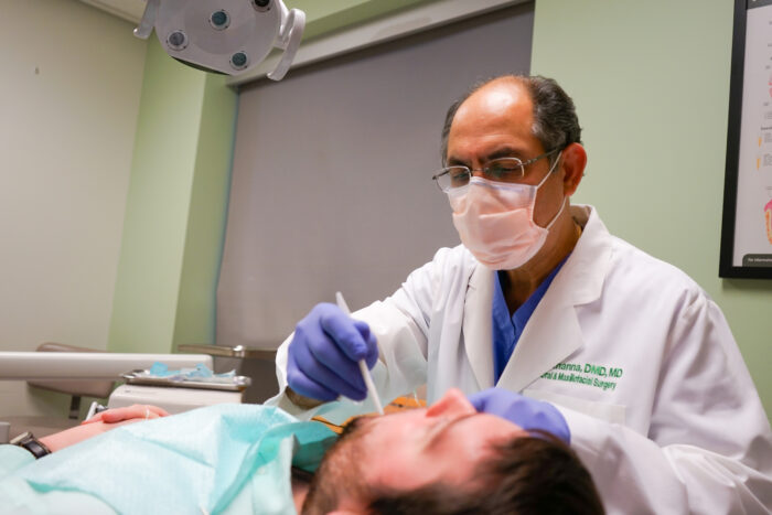 A candid photo a male dental surgeon working in a patient's mouth. The patient is male and facing away from the camera.