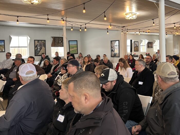 People are seated in several aisles of a farmhouse, looking forward.