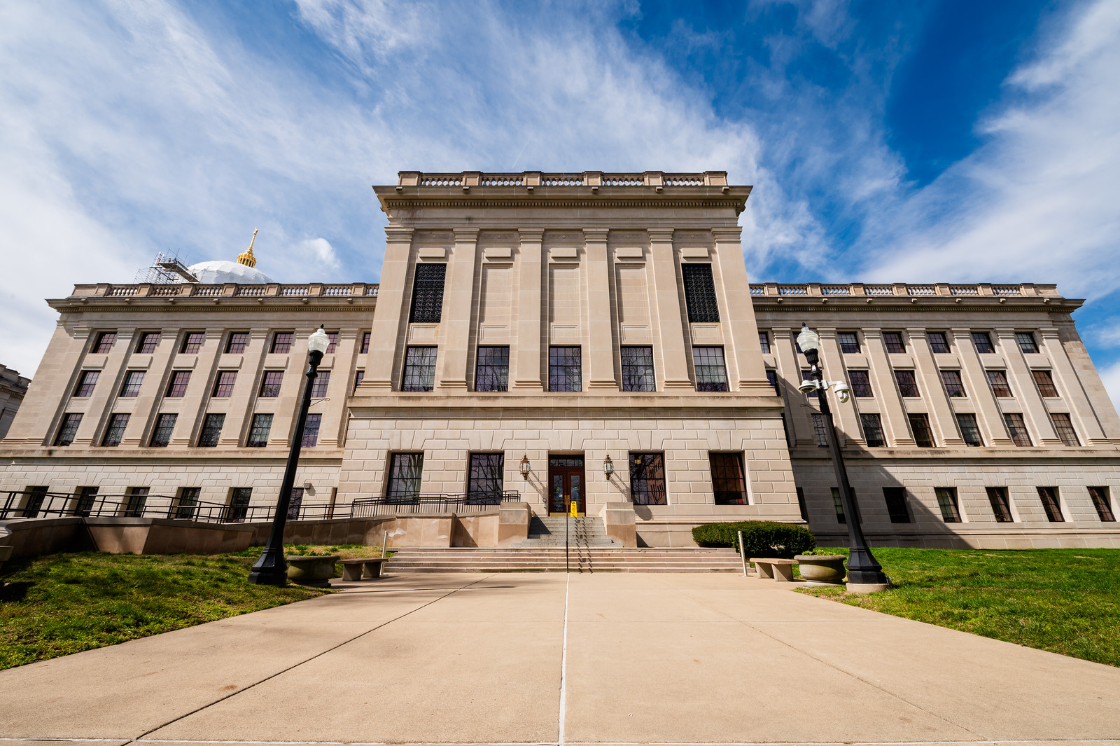 A four-story building with tan-colored bricks and many windows sits at the end of a sidewalk.