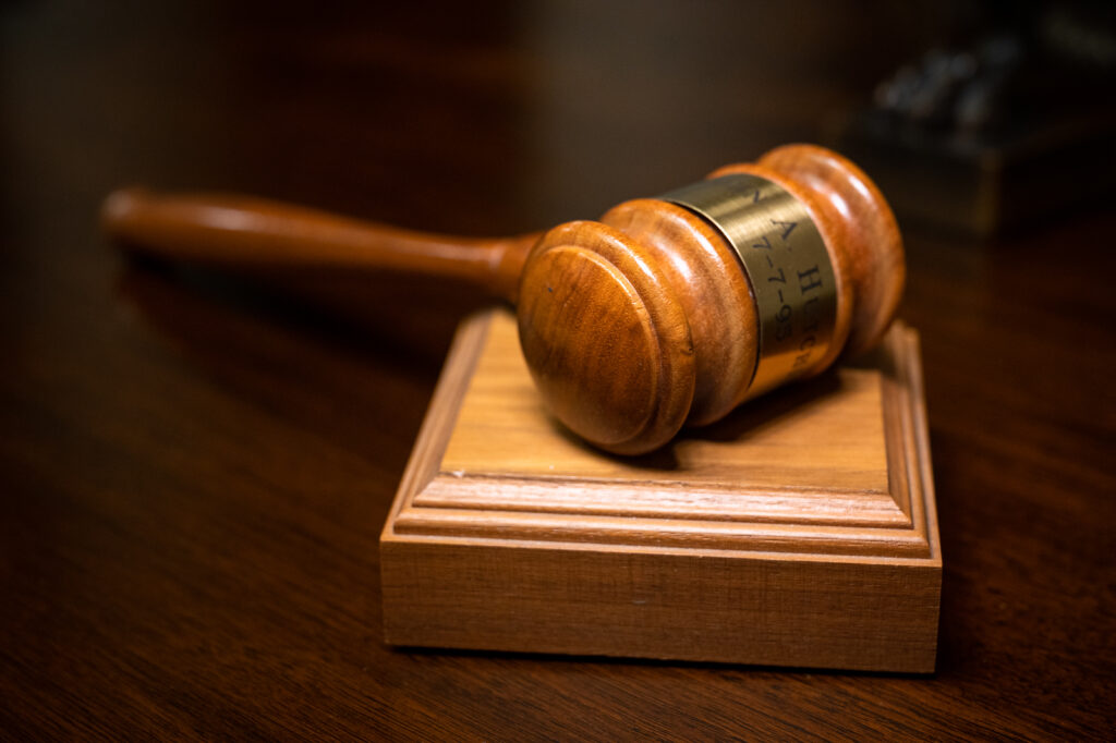 A hardwood gavel rests on a wooden block atop a desk.