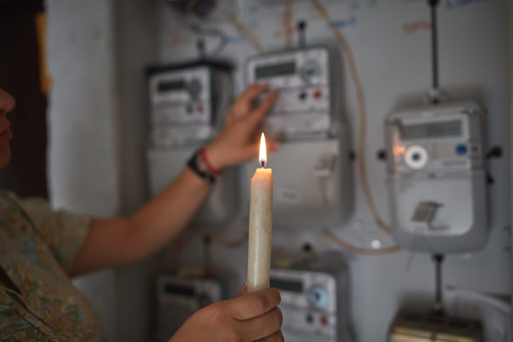 A pair of Caucasian hands holding a burning candle Checking the electricity power meter with a candle in cold winter days while there is power outage.
