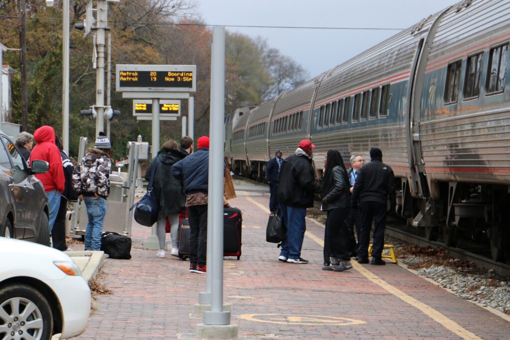 A group of passengers prepares to board a train on a brick station platform on a gray winter day.