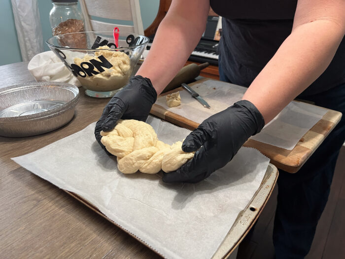 A woman wearing black, latex gloves places dough on a lined baking sheet.