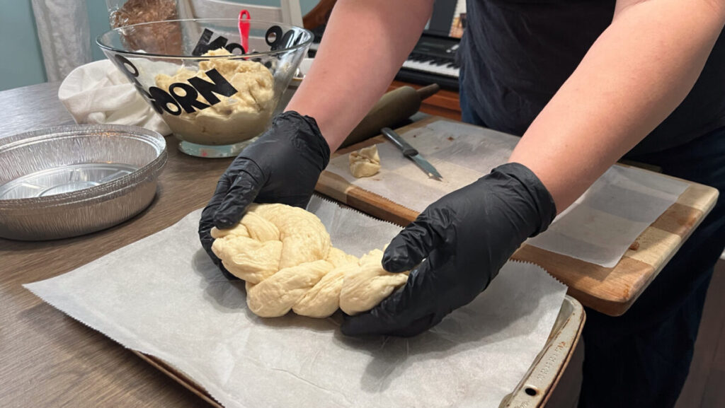A woman wearing black, latex gloves places dough on a lined baking sheet.