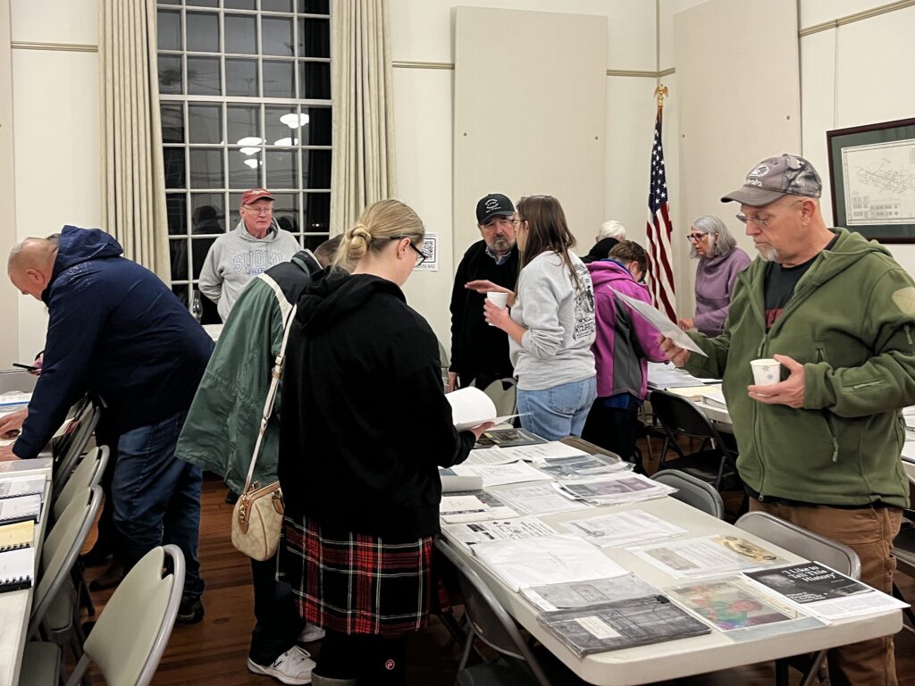 People stand at tables covered in pieces of paper and browse the documents, some picking up the materials laid out.