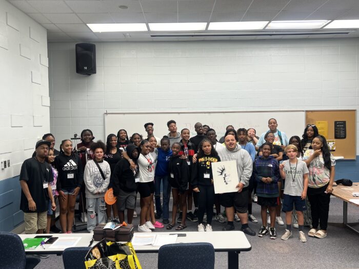 Dozens of young people stand together in a classroom posing for a photo.