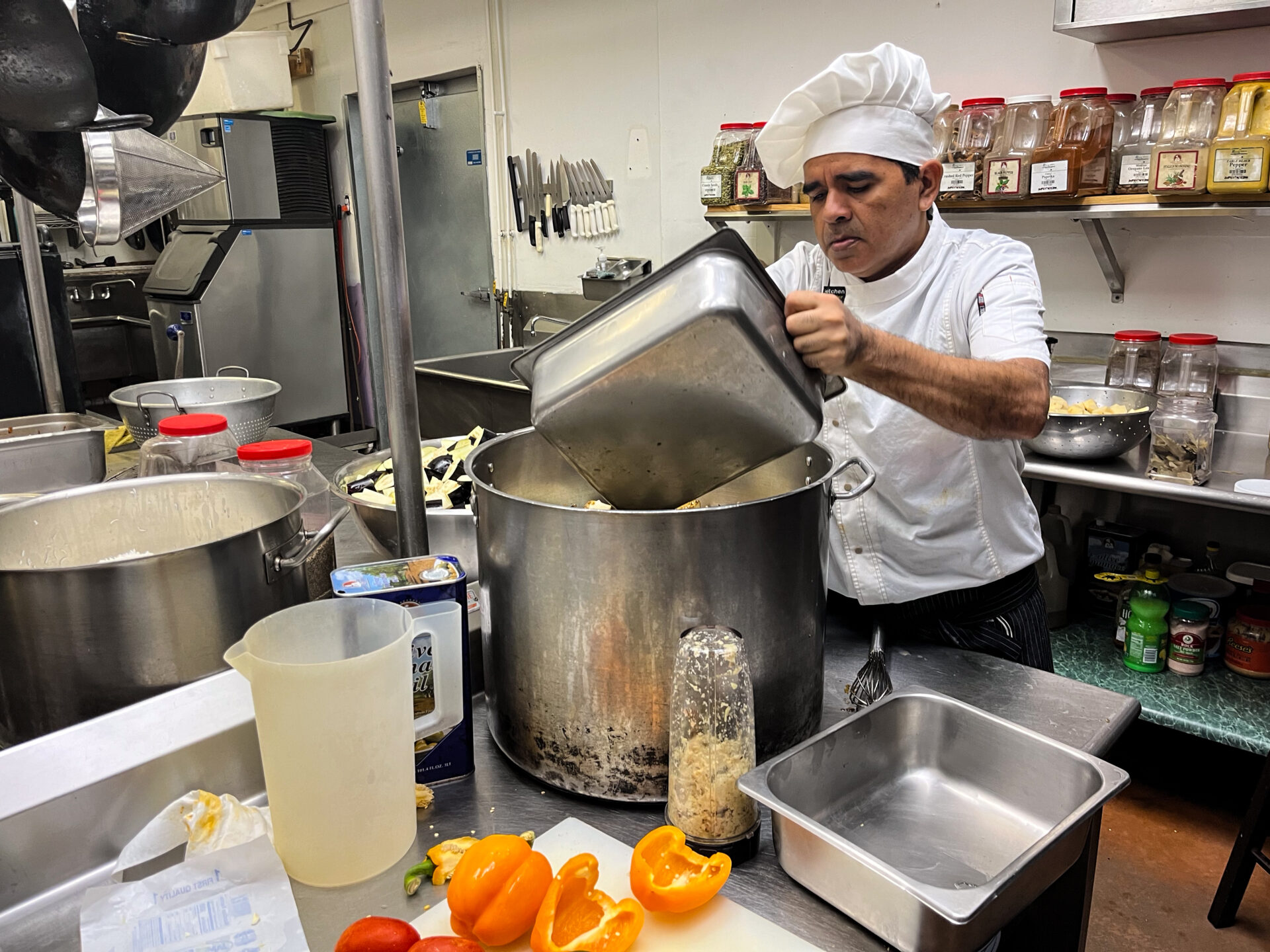 A man pouring food into a big pot on a counter in a kitchen.