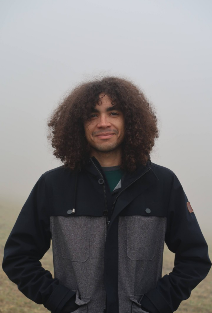 A person standing outside surrounded by fog and wearing a black and gray jacket.